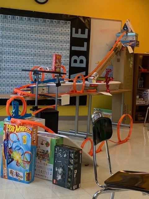 A classroom roller coaster project made with orange toy-car tracks, loops, and elevated ramps