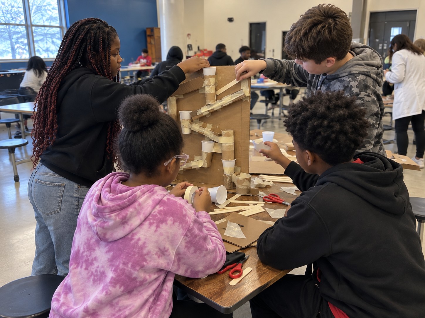 Students building a cardboard marble run, viewed from the side and behind